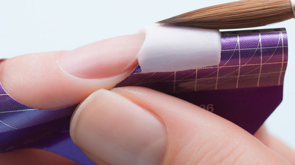 Nail tech building a nail with white acrylic on a nail form